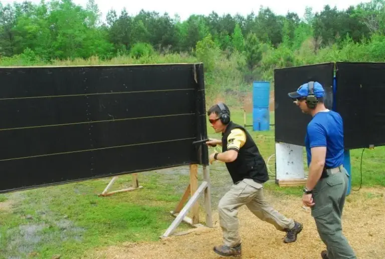 An IDPA competitor moving between barricades with a safety officer behind
