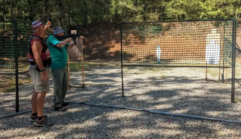 Shooters at the firing line of a pistol bay with target stands and mesh fence