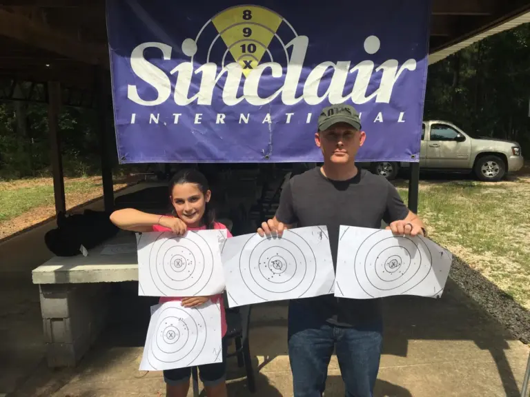 Two shooters holding up their targets under the Sinclair banner